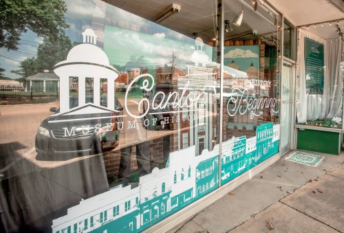 Window display of the Camden Museum of History, featuring a graphic of a historic building and the text "Camden Beginnings."