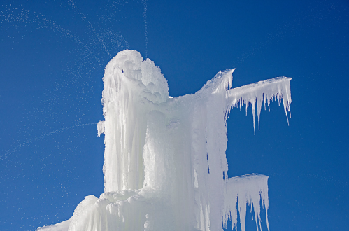 A tall ice formation with icicles against a clear blue sky, sparkling in the sunlight.