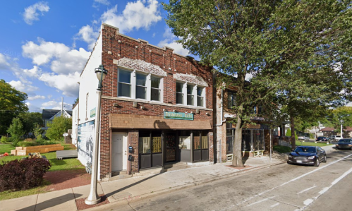 A brick building with a sign reading "The Local Café," surrounded by trees and a clear blue sky.