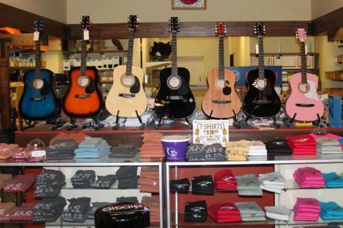 A display of colorful guitars and folded t-shirts in a shop, showcasing various merchandise for sale.