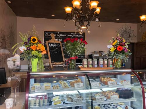 A cozy café display featuring a glass case of pastries, a chalkboard menu, and vibrant flower arrangements.