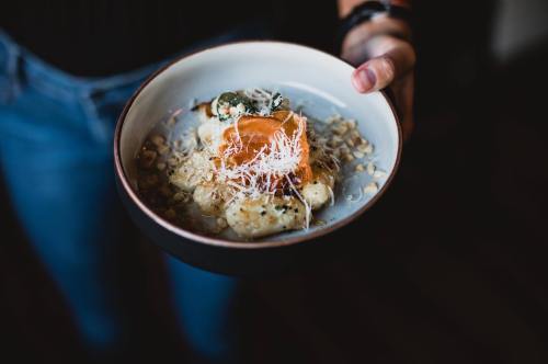 A person holding a bowl of gnocchi topped with cheese and garnishes, served on a textured plate.