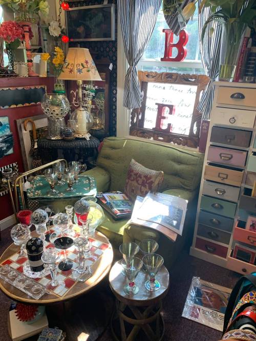 A cozy, eclectic room filled with colorful decor, vintage furniture, and various glassware on tables.
