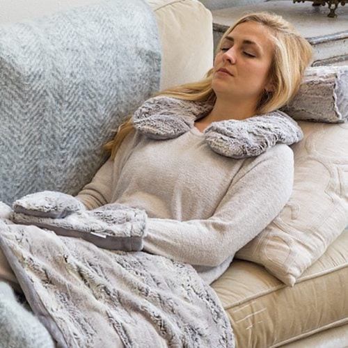 A woman relaxes on a couch, wearing a cozy gray sweater and a soft neck wrap, with her eyes closed.