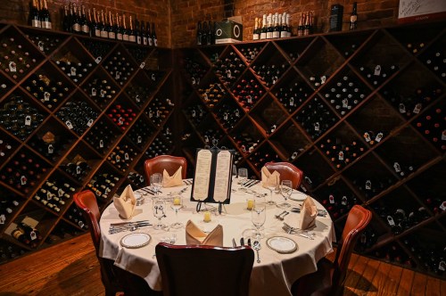 A round dining table set for a meal, surrounded by wine racks filled with various bottles in a cozy restaurant.