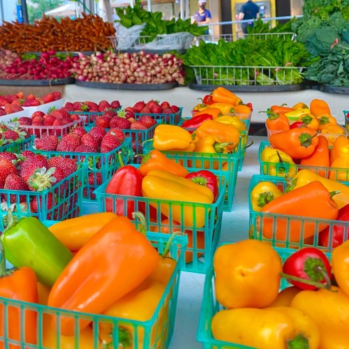 Colorful baskets of strawberries and mini bell peppers at a vibrant farmers market. Fresh produce on display.