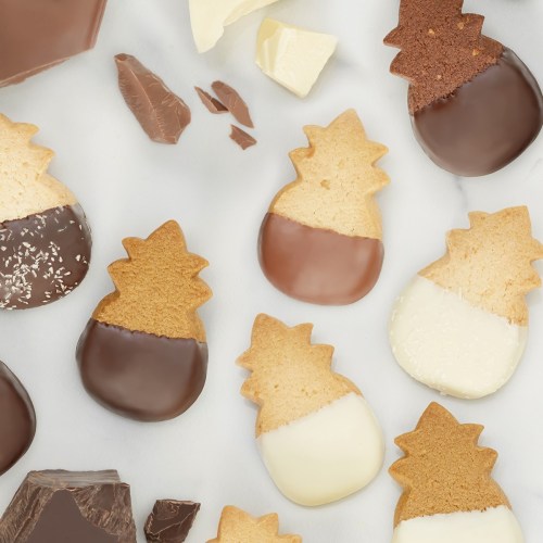 A variety of pineapple-shaped cookies, some dipped in dark, milk, and white chocolate, scattered on a marble surface.