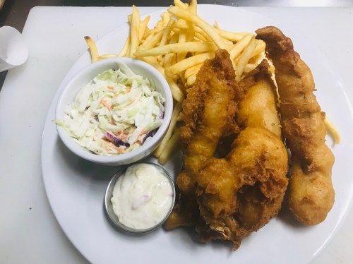 A plate of fried fish fillets, French fries, coleslaw, and a small cup of tartar sauce.