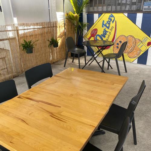 A wooden table with black chairs in a bright outdoor space featuring a mural and potted plants.