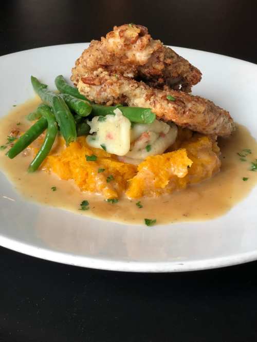 A plate of fried shrimp atop mashed sweet potatoes, green beans, and gravy, garnished with parsley.