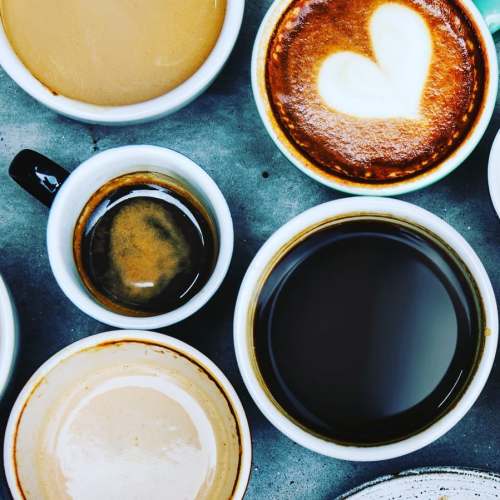 A variety of coffee cups with different types of coffee, including a latte with a heart design, arranged on a table.