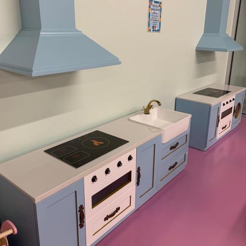 A colorful play kitchen setup featuring a sink, stove, and oven against a light blue wall.