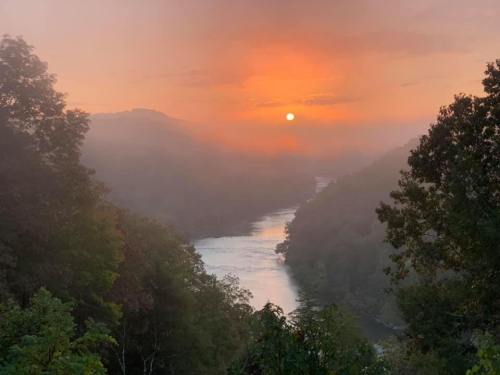 A serene river landscape at sunrise, shrouded in mist with trees framing the view and soft orange hues in the sky.