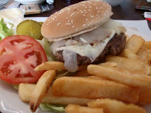 A sesame seed bun burger with cheese, onions, lettuce, and tomato, served with a side of golden French fries.