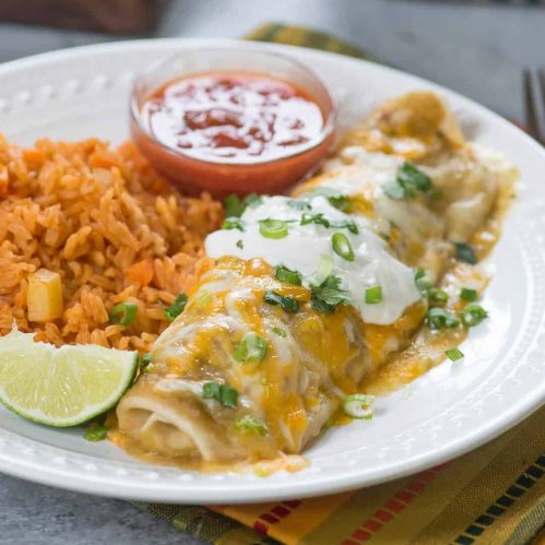 A plate of enchiladas topped with cheese and sour cream, served with rice and a side of salsa.