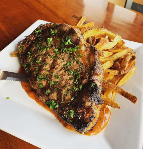 A juicy grilled steak topped with herbs, served with crispy fries on a white plate.