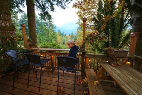 An elderly person sits on a deck surrounded by trees and mountains, with autumn leaves scattered around.