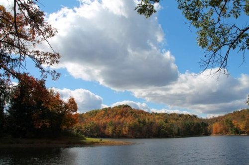 A serene lake surrounded by colorful autumn trees under a bright blue sky with fluffy clouds.