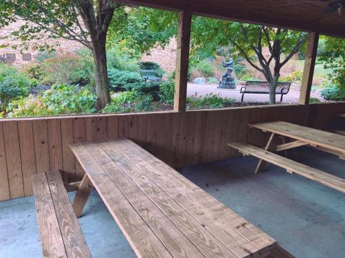 A wooden picnic area with benches overlooks a garden featuring trees and a statue in the background.