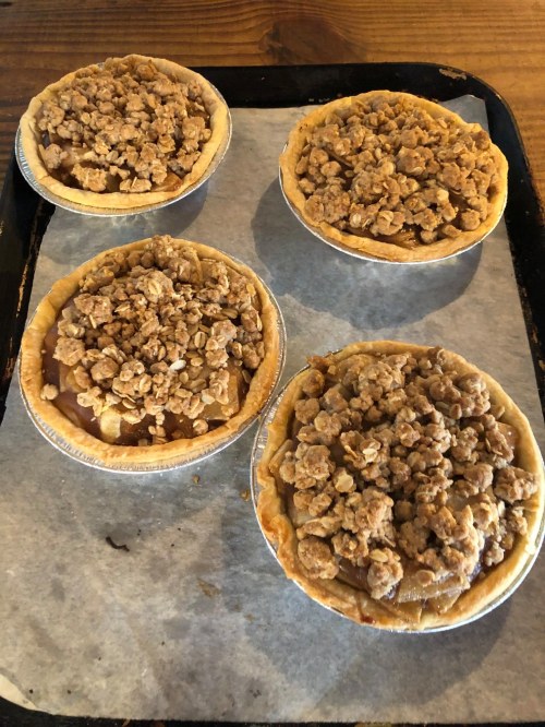 Four mini pies on a baking tray, each topped with a crumbly oat topping.
