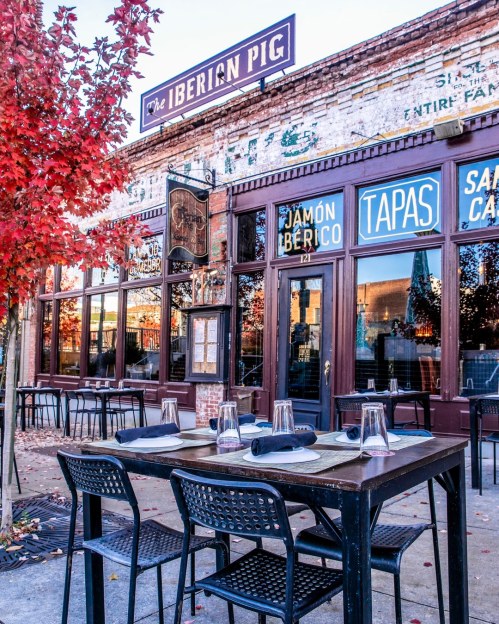 Outdoor dining setup at The Iberian Pig, featuring tables, chairs, and vibrant fall foliage.