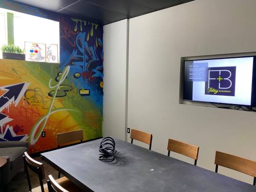 A modern meeting room with a colorful mural, a large table, and a screen displaying a logo.
