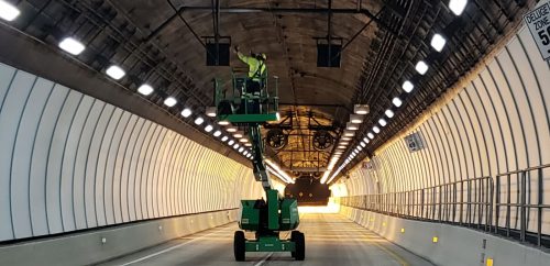 A worker in a lift performs maintenance inside a brightly lit tunnel.