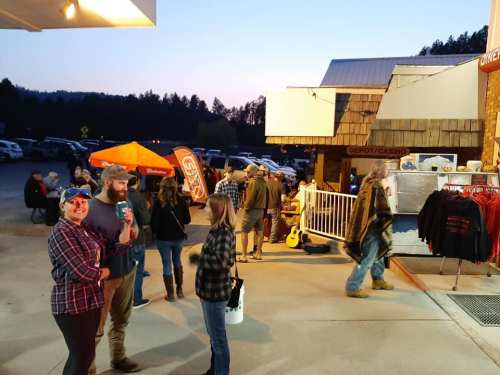 A lively outdoor scene at a casino with people socializing, merchandise for sale, and a sunset in the background.