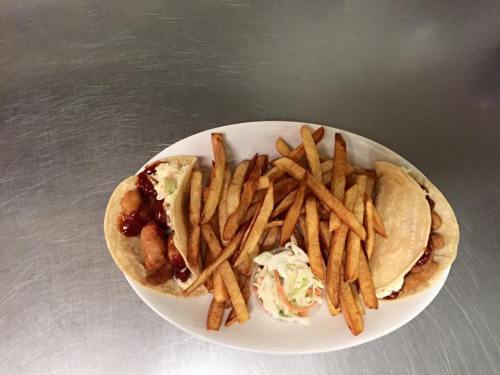 A plate of two tacos filled with meat and sauce, accompanied by a side of crispy fries and coleslaw.