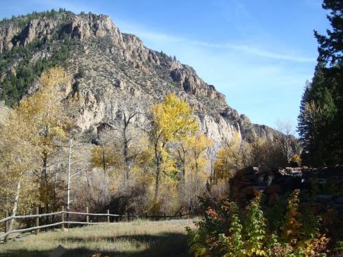 Scenic view of a mountain with autumn foliage and a wooden fence in the foreground under a clear blue sky.