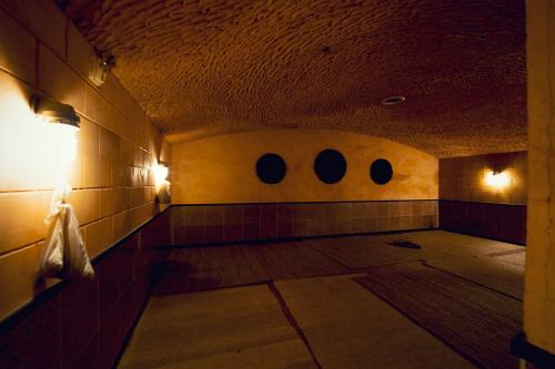 A dimly lit, rustic room with textured walls, circular wall features, and a woven mat floor.