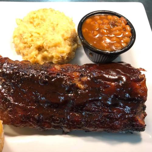 A plate featuring BBQ ribs with a glossy sauce, creamy mashed potatoes, and a side of baked beans.