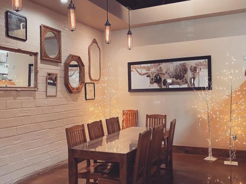 A cozy dining area with a wooden table, chairs, decorative mirrors, and warm lighting from pendant lamps and fairy lights.