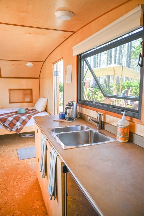 Cozy interior of a tiny cabin with a kitchen sink, coffee maker, and a view of trees through the window.