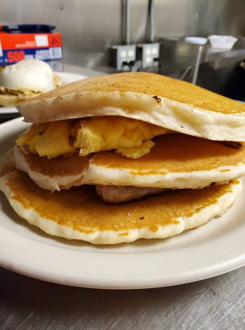 A stack of fluffy pancakes filled with scrambled eggs and served on a white plate.