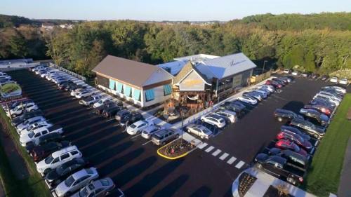Aerial view of a restaurant with a large parking lot filled with cars, surrounded by trees and greenery.