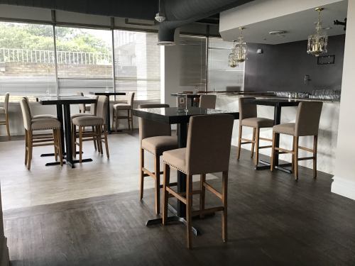 A modern, stylish bar area with high tables and chairs, large windows, and elegant lighting fixtures.