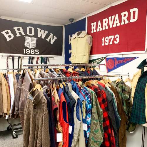 A clothing rack filled with various jackets and vests, with Brown and Harvard banners hanging on the wall above.