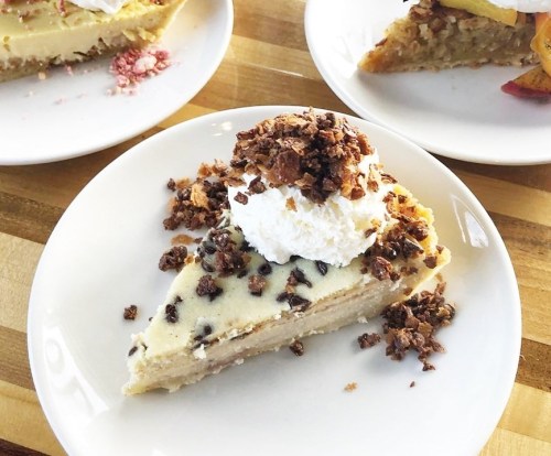 A slice of creamy dessert topped with whipped cream and crunchy toppings, served on a white plate.