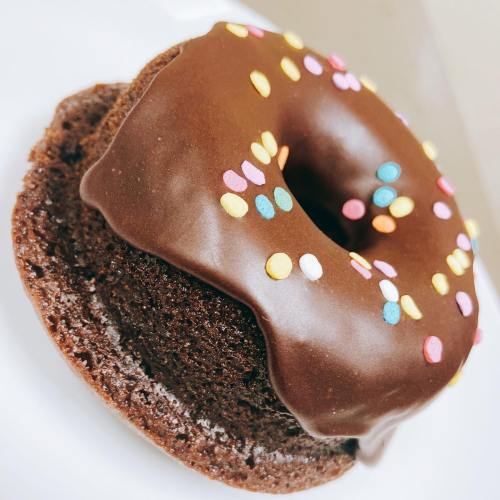 A chocolate frosted donut topped with colorful sprinkles on a white plate.
