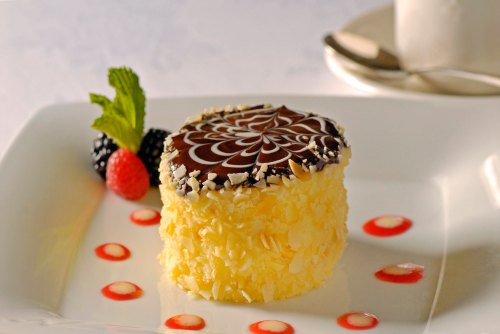 A round dessert topped with chocolate and decorated with berries and sauce on a white plate.