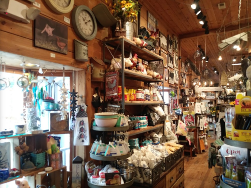 A cozy shop interior filled with various home decor items, kitchen supplies, and rustic decorations on wooden shelves.
