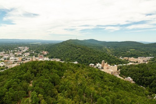 Aerial view of a lush green landscape with hills, a town below, and a cloudy sky in the background.