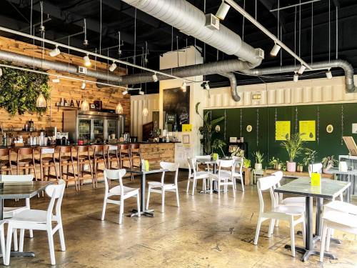 Bright, modern café interior with wooden accents, green walls, and white furniture, featuring plants and a bar area.