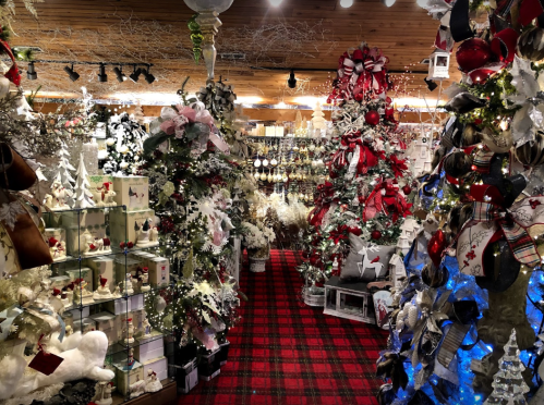 A festive shop filled with Christmas decorations, including trees, ornaments, and ribbons, all in a cozy, warm setting.