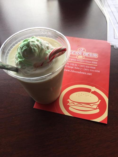 A festive milkshake topped with whipped cream and a candy cane, next to a restaurant menu on a wooden table.