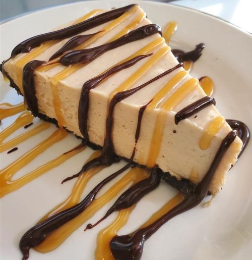 A slice of creamy dessert topped with chocolate and caramel sauce on a plate.