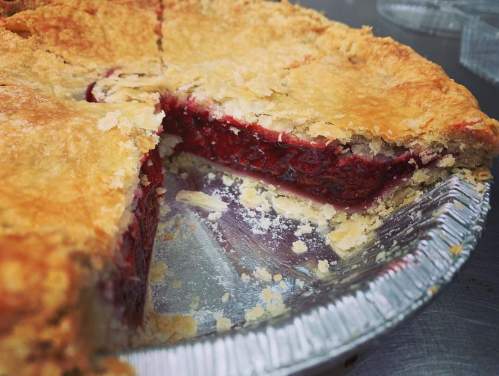 A close-up of a freshly baked pie with a flaky crust and a slice removed, revealing a rich, red filling.