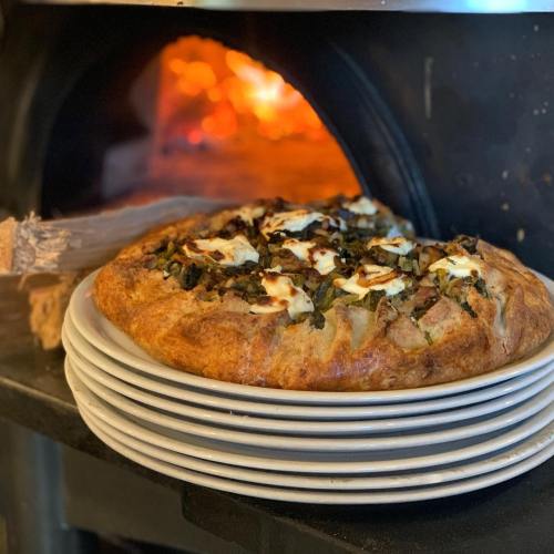A freshly baked savory pie with greens and cheese, placed in front of a wood-fired oven.