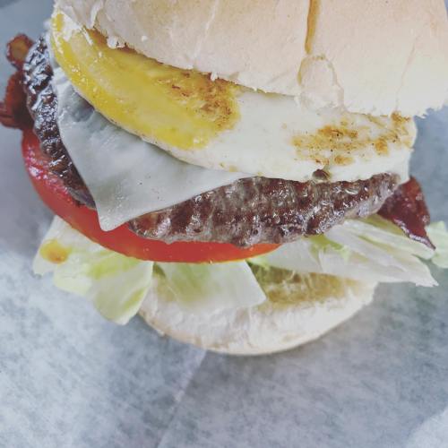 A close-up of a burger with a beef patty, cheese, fried egg, lettuce, tomato, and a soft bun.